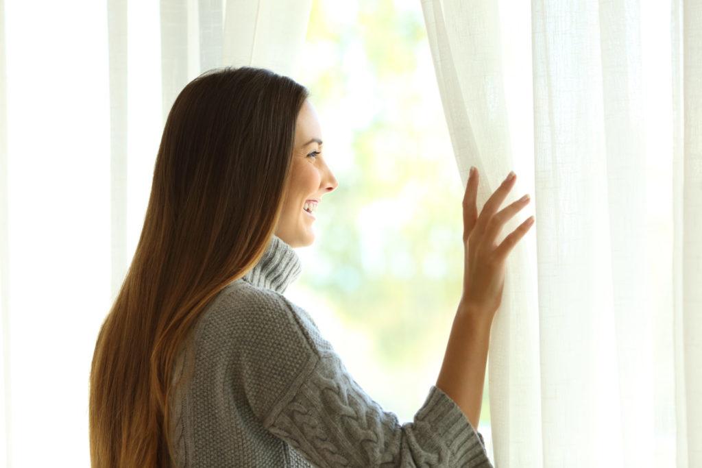 Kyptonitmensch Frau schaut lächelnd aus einem Fenster