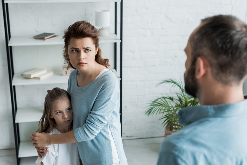 Parentifizierung in Aktion: Eine misstrauisch blickende Mutter legt schützend die Hände um ihr Kind, während der Vater sie ansieht.