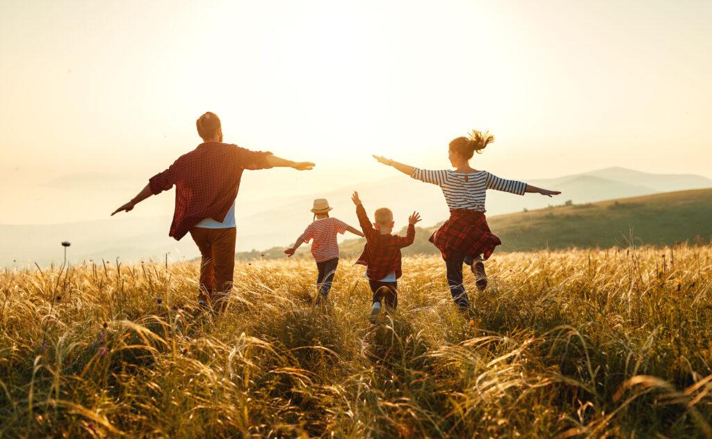 Eine glückliche Familie tanzt durch ein Kornfeld im Sonnenuntergang.